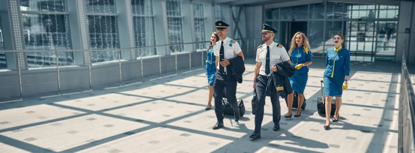 Airline pilots and cabin crew in uniform walking through an airport with luggage
