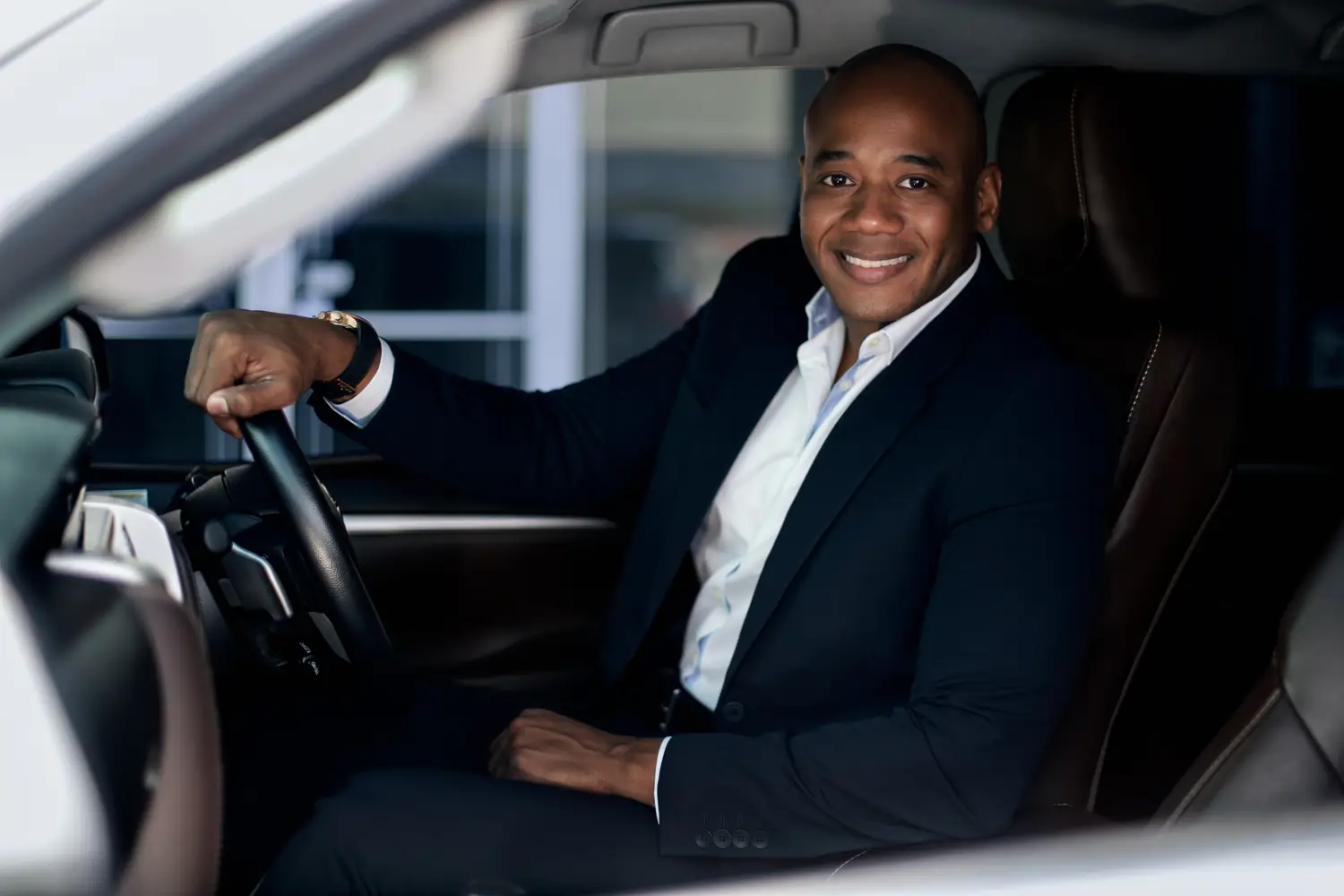 Professional chauffeur in a suit smiling from the driver's seat