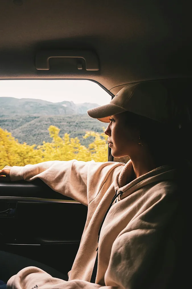 Passenger in a cap relaxing in a car, looking out at mountain scenery